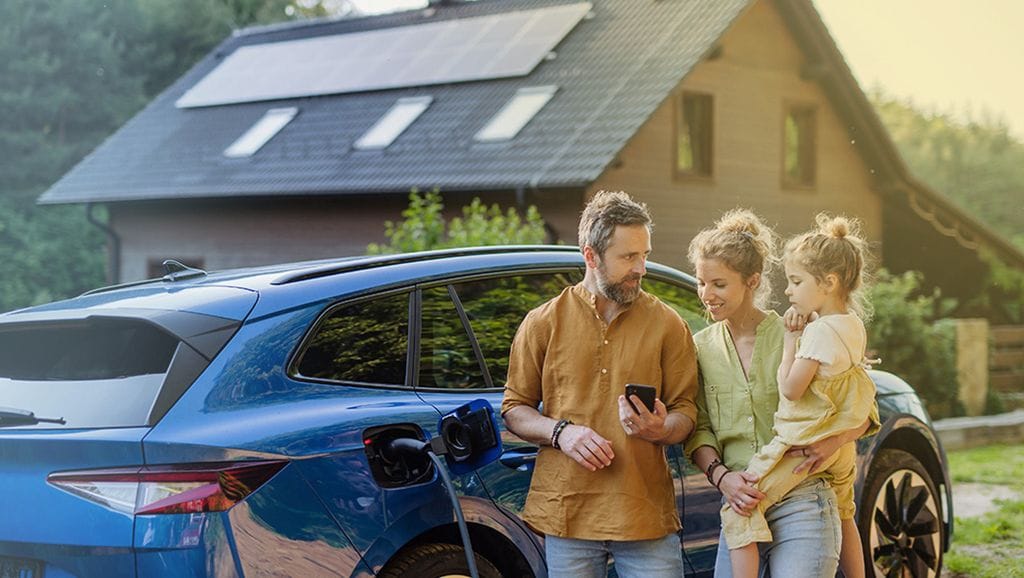 Family standing beside an EV that is charging, near a solar-paneled house