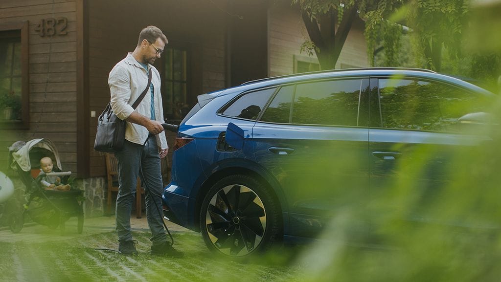 Man is charging his electric vehicle in front of a house with a baby in a stroller nearby