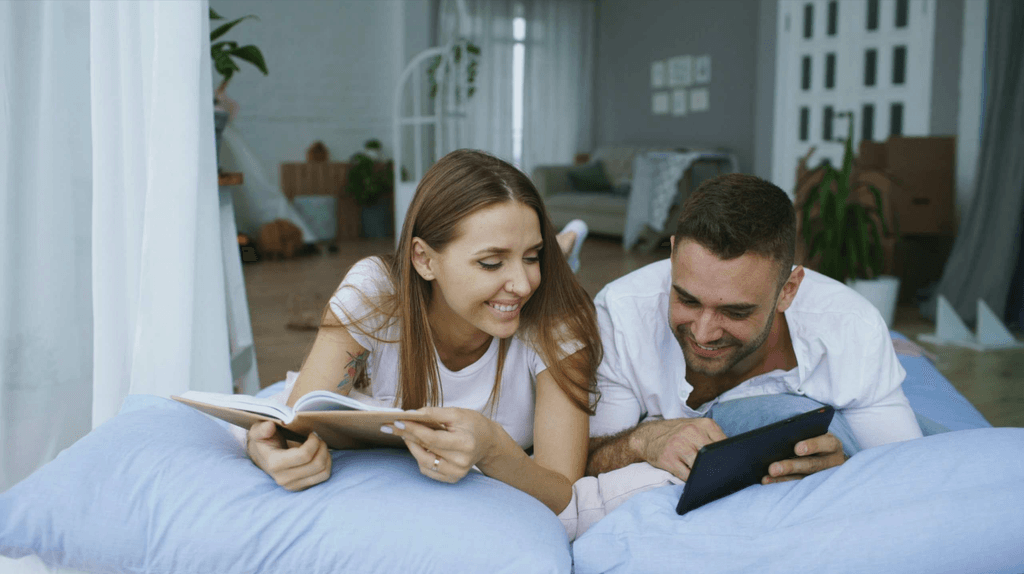 Couple on couch reading and using tablet while laughing